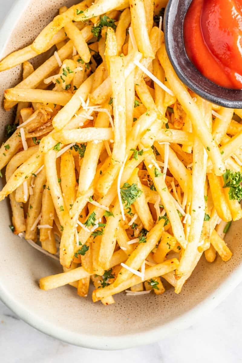garlic parmesan fries in a white bowl with ketchup.