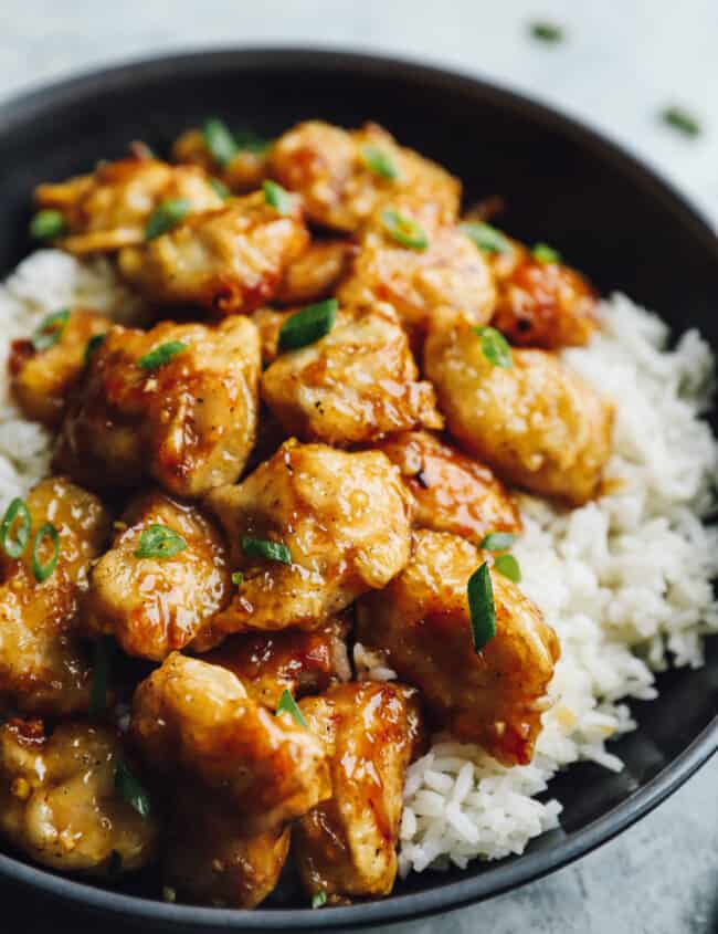 honey chicken over white rice in a black bowl.