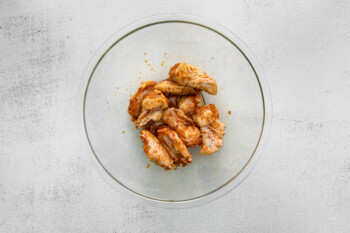 chicken wings tossed in dry rub in a glass bowl.