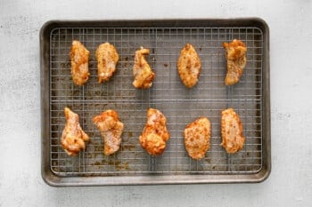 raw dry rubbed chicken wings on a wire rack set in a baking sheet.