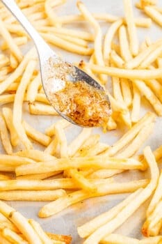 garlic parmesan butter spooned over baked french fries on a sheet pan.