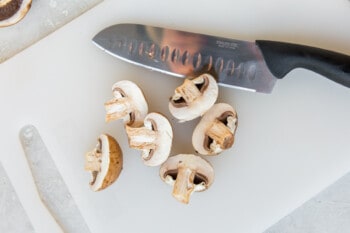 sliced mushrooms on a white cutting board with a knife.