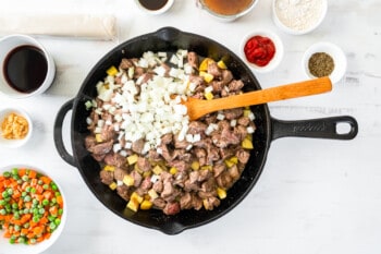 onion added to potatoes and beef in a skillet with a wooden spoon.