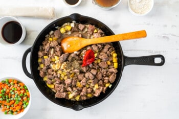 tomato paste added to beef mixture in a skillet with a wooden spoon.