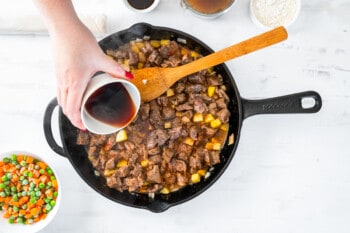 worcestershire sauce added to beef mixture in a skillet with a wooden spoon.