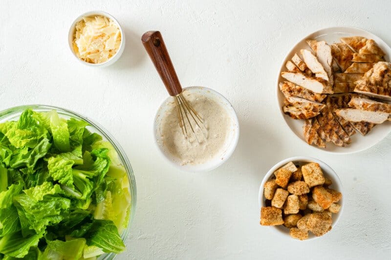 chicken caesar salad dressing in a white bowl with a whisk.