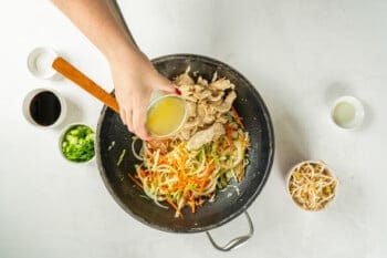 chicken broth added to stir fried meat and vegetables in a frying pan.