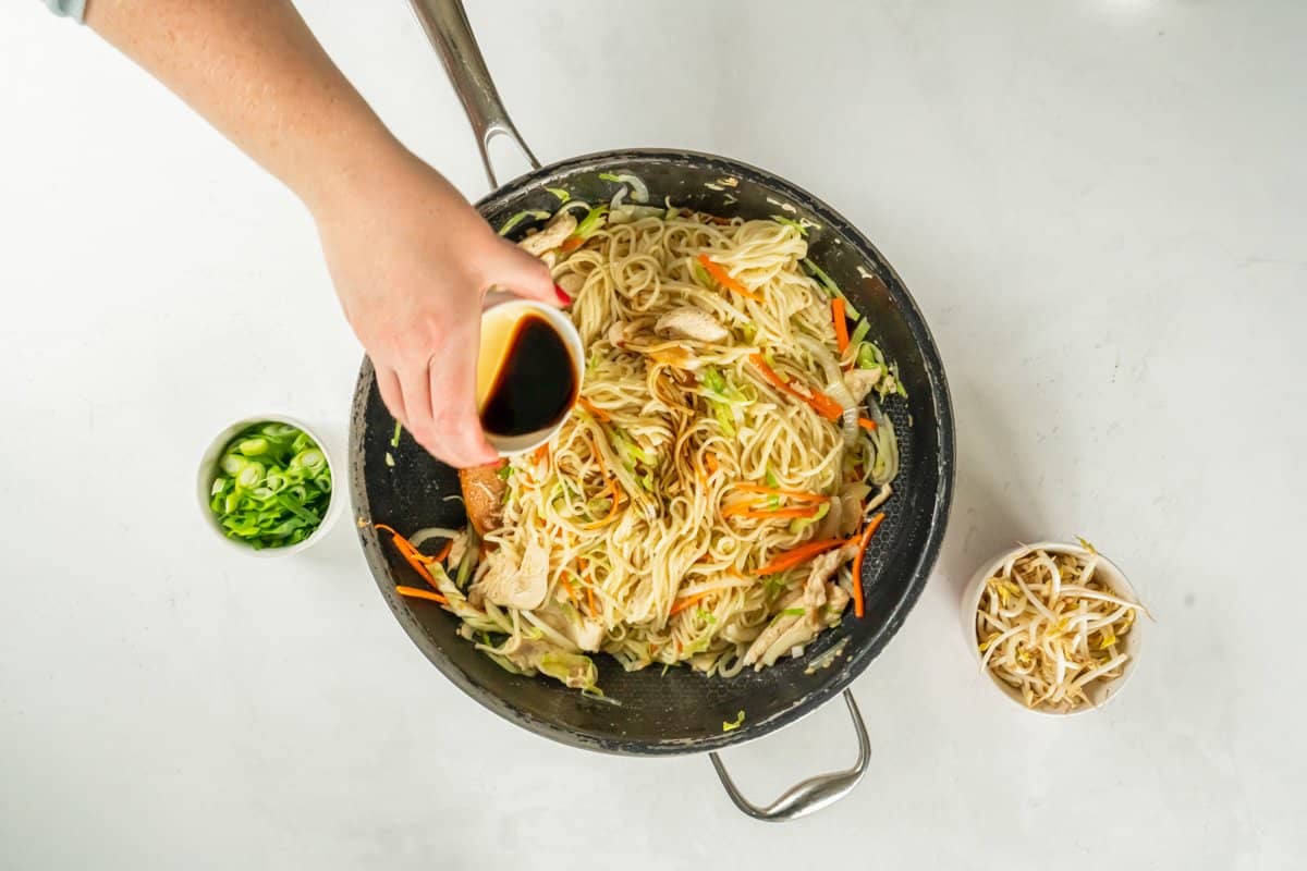 Soy sauce added to chicken lo mein in a frying pan. - 12