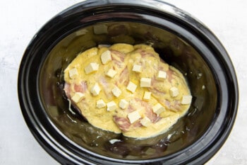 cream cheese cubes nested into chicken with ranch sauce in a crockpot.