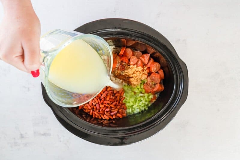 chicken broth poured over ingredients for red beans and rice in a crockpot.