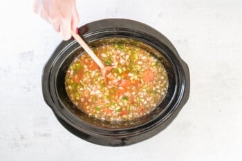 uncooked red beans and rice stirred with a wooden spoon in a crockpot.