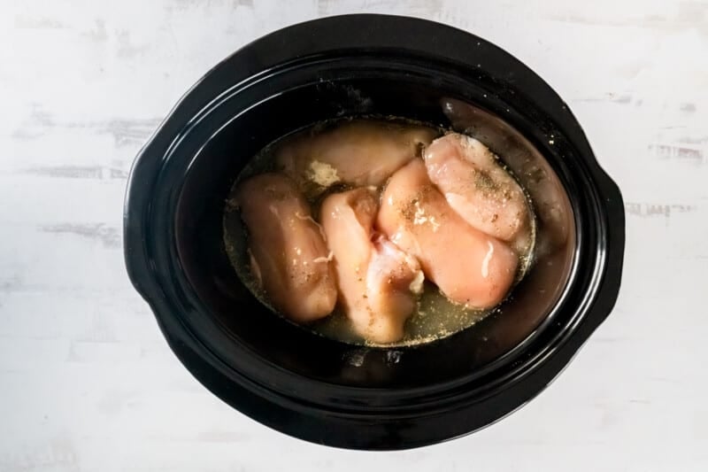 seasoned chicken breasts and broth in a crockpot.