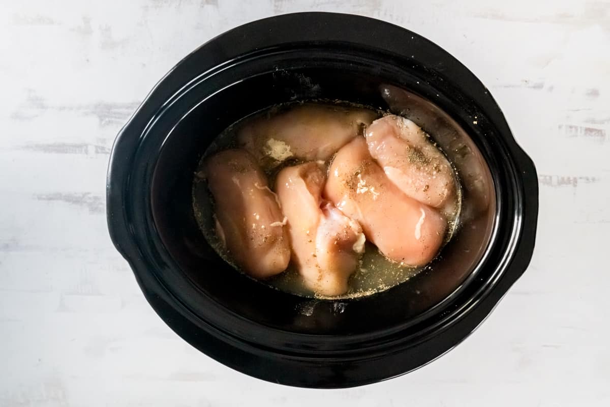 Seasoned chicken breasts and broth in a crockpot.