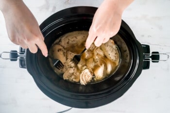 hands shredding crockpot chicken breasts with two forks.