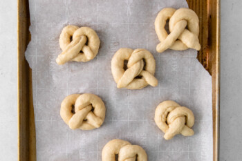 shaped garlic parmesan soft pretzels on a baking sheet.