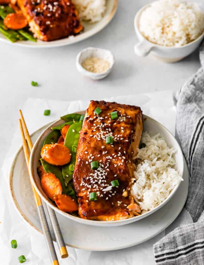 air fryer miso salmon in a white bowl with rice carrots and snap peas.