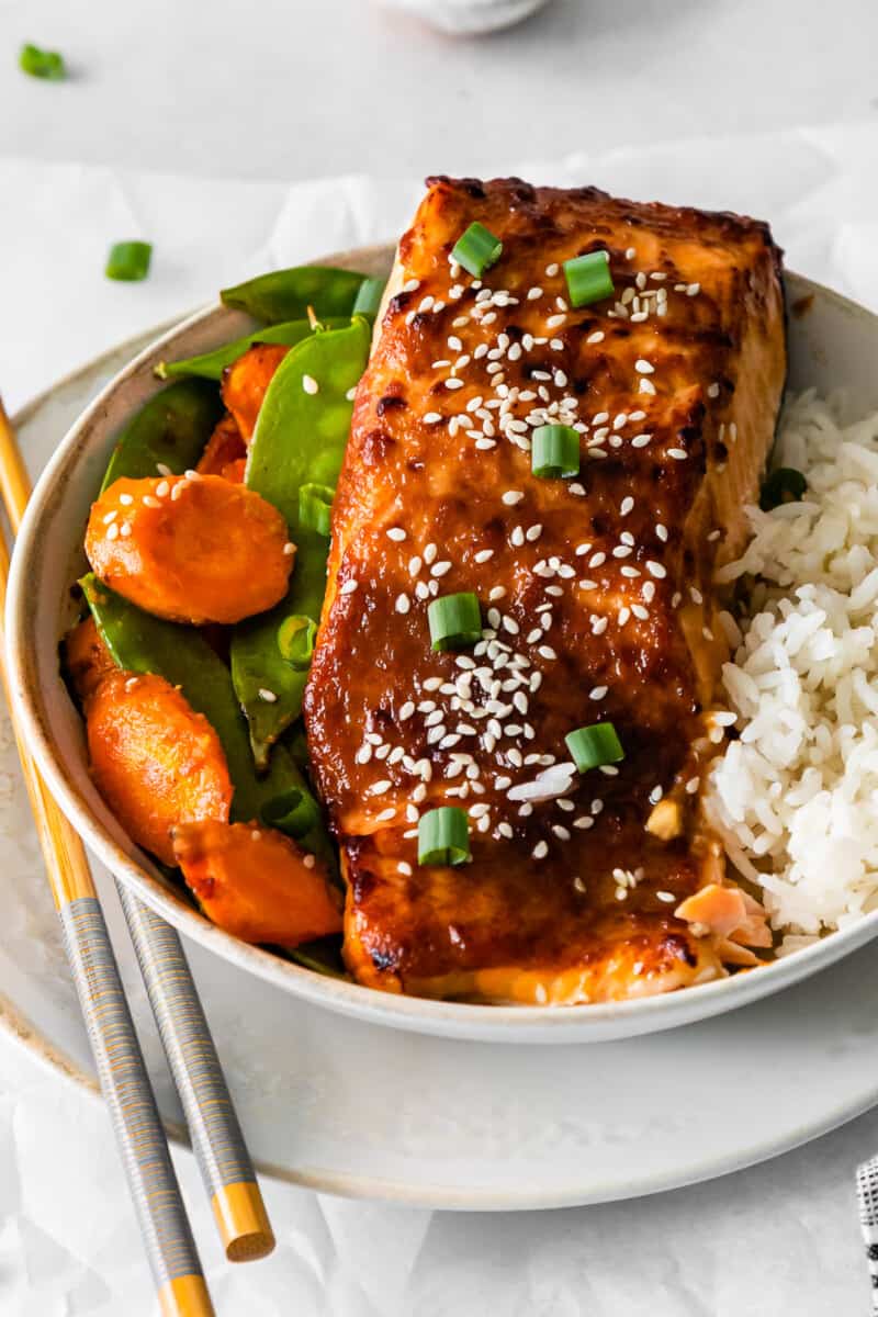 air fryer miso salmon in a white bowl with rice carrots and snap peas.