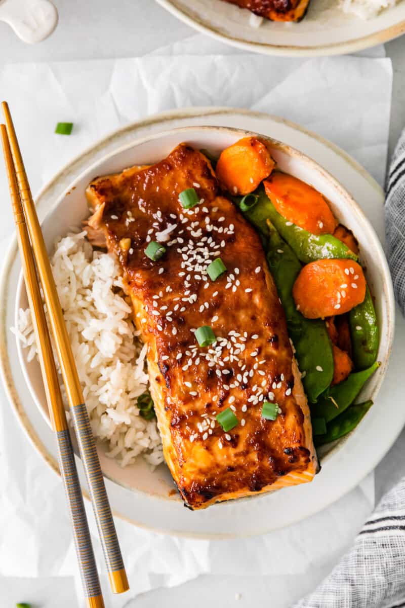 chopsticks resting on a bowl of air fryer miso salmon with rice carrots and snap peas.