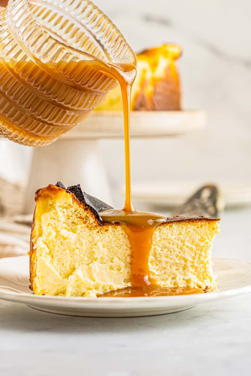 caramel poured over a slice of basque cheesecake on a white plate.