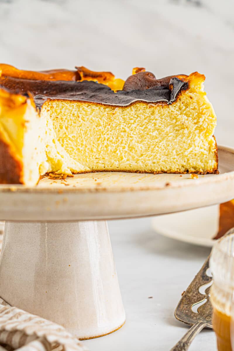 a sliced basque cheesecake on a white cake stand.