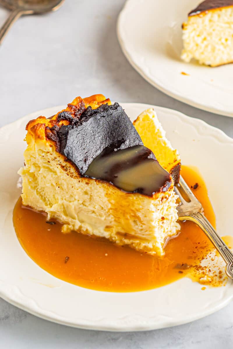 a forkful of basque cheesecake resting on a plate with a slice doused in caramel.
