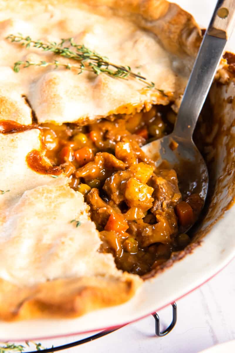 sliced beef pot pie in a pie pan with a serving spoon.