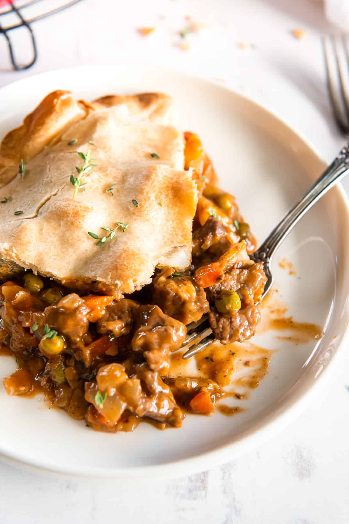 a slice of beef pot pie on a white plate with a fork.