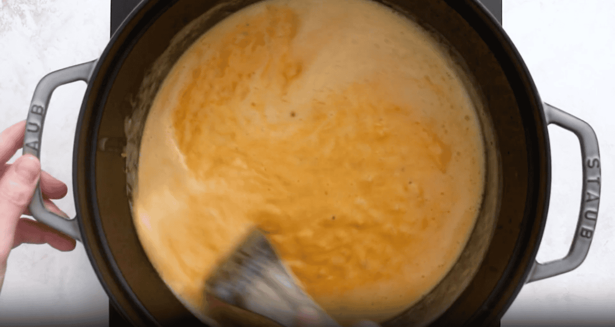 beer cheese soup in a dutch oven with a wooden spoon.