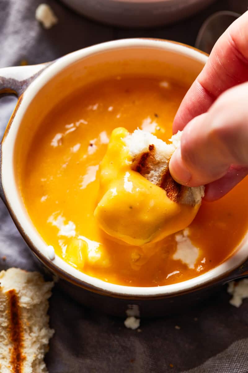 This Beer Cheese Soup recipe is so delicious and made in just 15 minutes! This creamy comfort food is the perfect winter dinner recipe. If you love cheese and beer (what could be better?), this easy beer cheese soup is just for you. dipping a piece of bread into a bowl of beer cheese soup