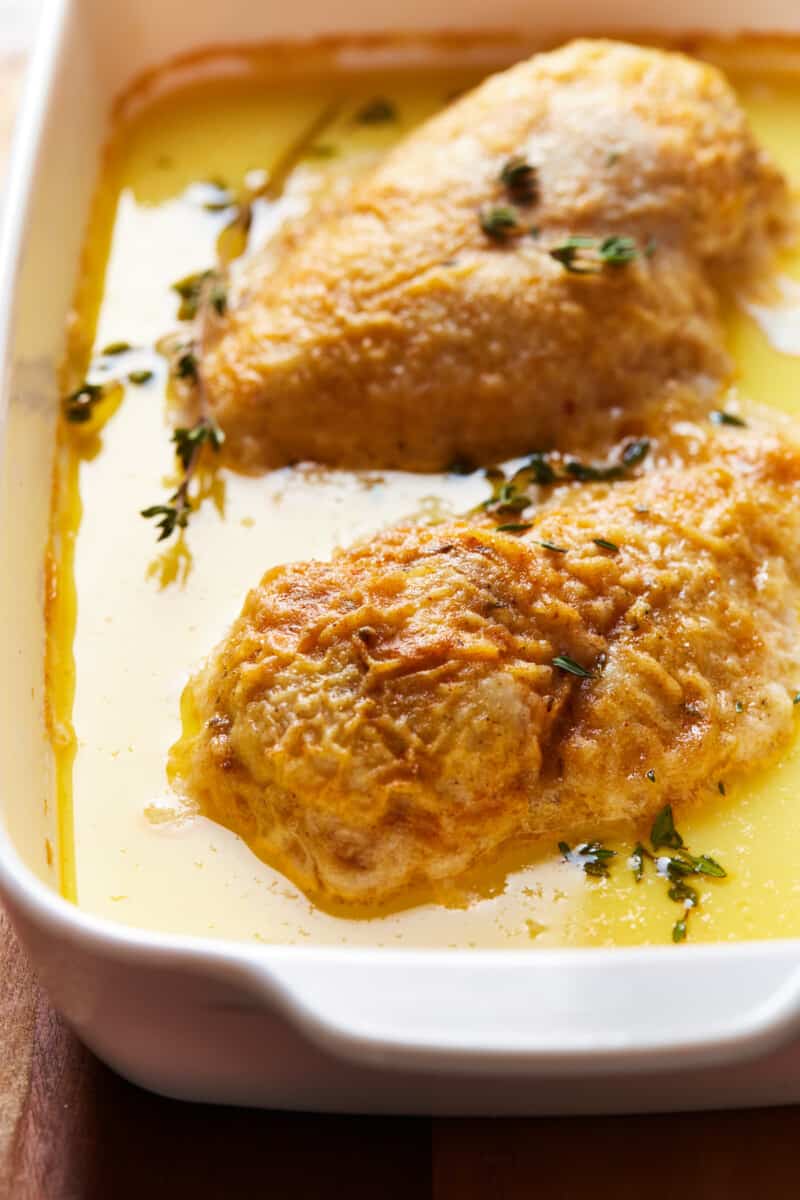 chicken in a baking dish surrounded by butter and cream