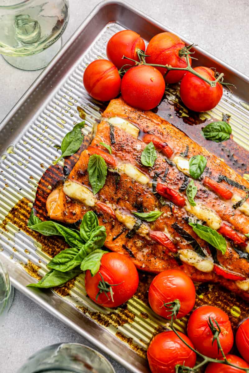This Caprese Stuffed Salmon recipe is cheesy, delicious, and made on one pan! Baked salmon stuffed with tomato & mozzarella, paired with balsamic tomatoes. stuffed salmon and tomatoes on a baking tray