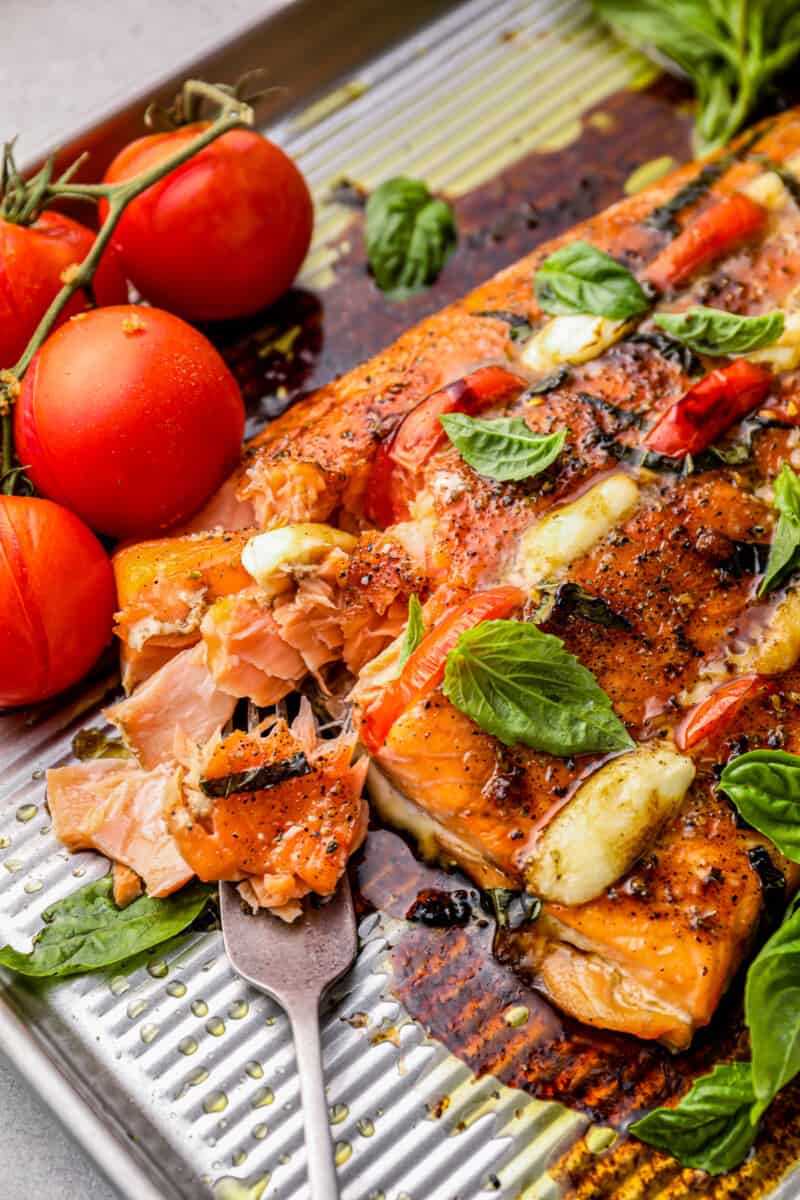 This Caprese Stuffed Salmon recipe is cheesy, delicious, and made on one pan! Baked salmon stuffed with tomato & mozzarella, paired with balsamic tomatoes. close up of caprese stuffed salmon on a baking tray
