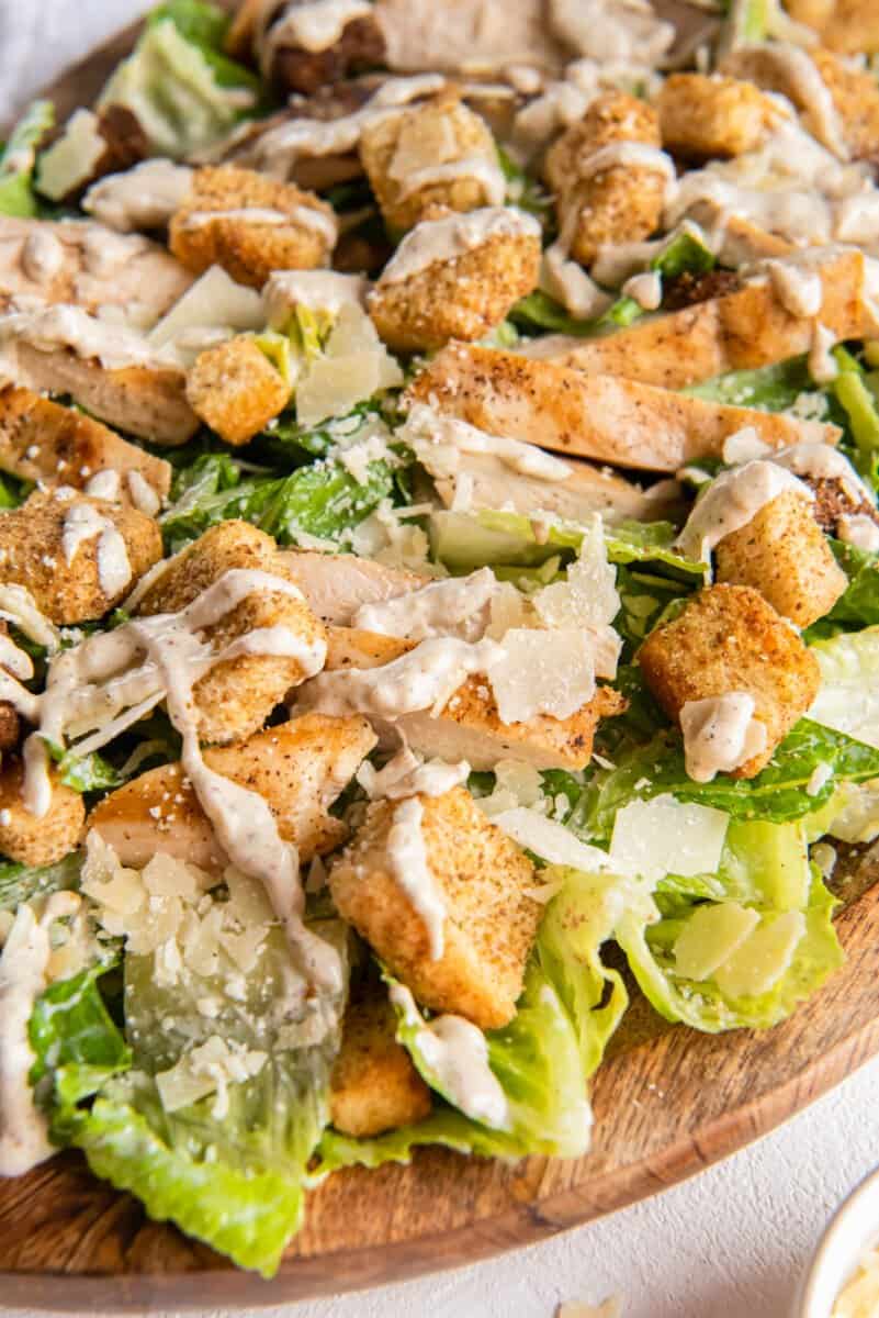 close up of chicken caesar salad in a wooden serving bowl.
