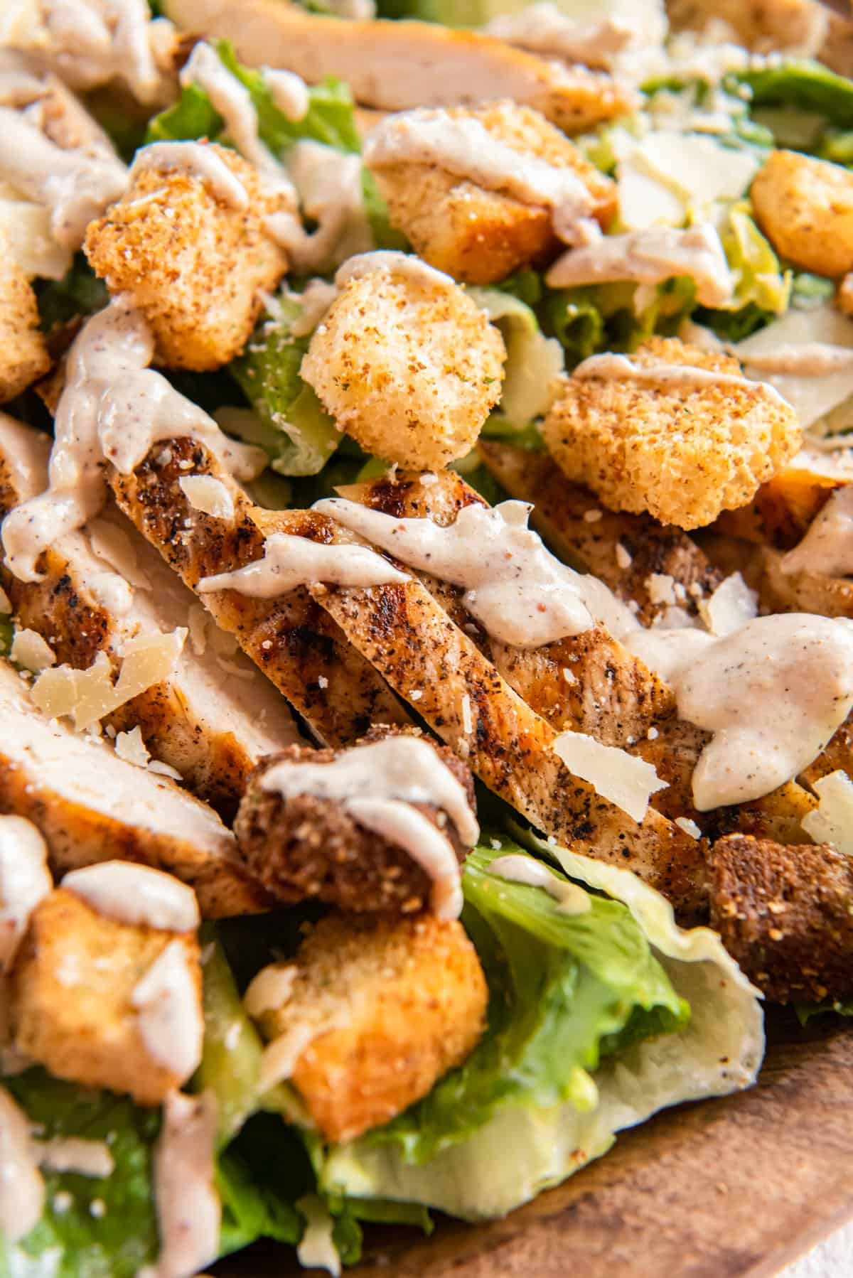 close up of chicken caesar salad in a wooden serving bowl.
