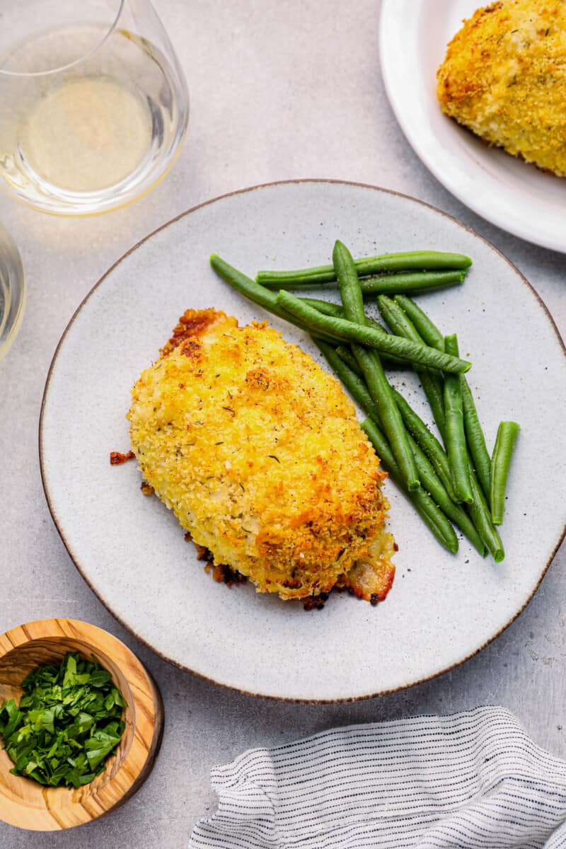 chicken cordon bleu baked on a white plate with green beans.