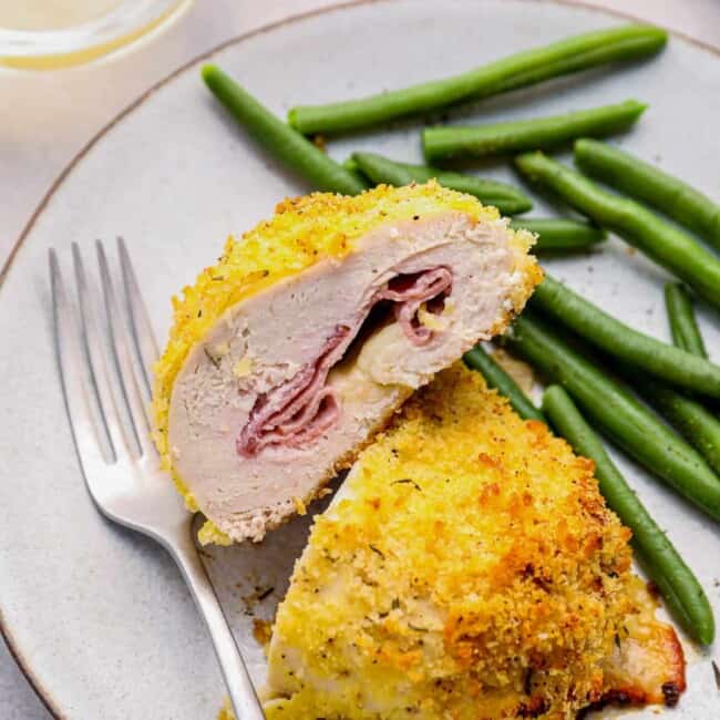 sliced chicken cordon bleu baked on a white plate with green beans and a fork.