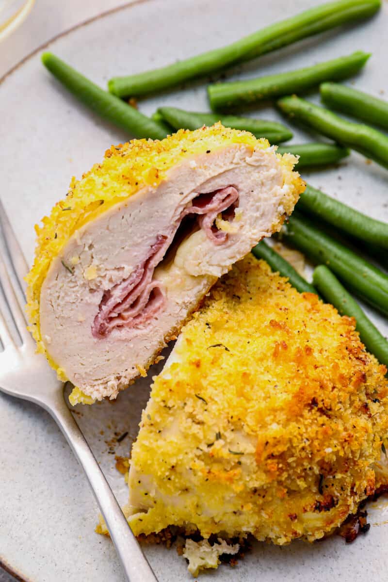 sliced chicken cordon bleu baked on a white plate with green beans and a fork