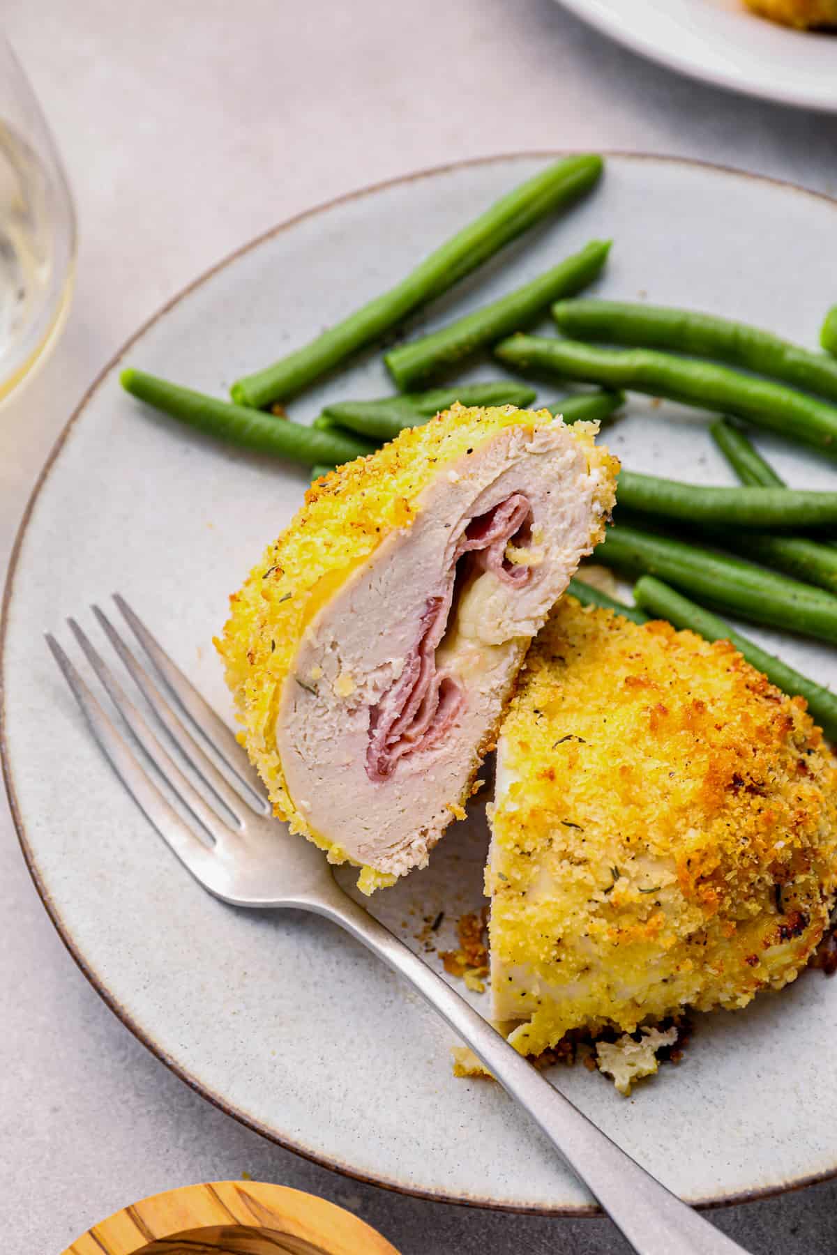 sliced chicken cordon bleu baked on a white plate with green beans and a fork.