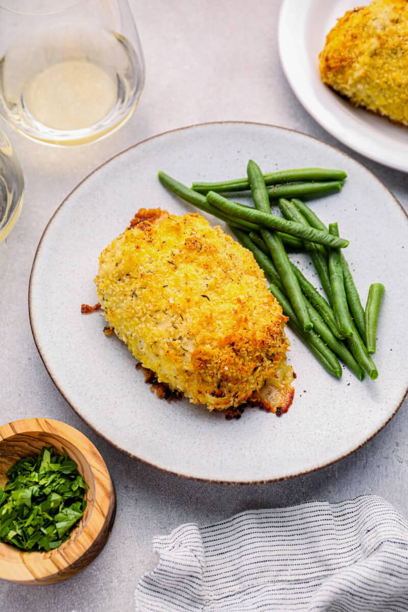 chicken cordon bleu baked on a white plate with green beans.