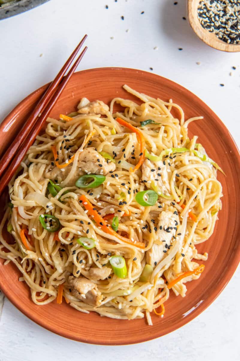 chicken lo mein on an orange plate with chopsticks.