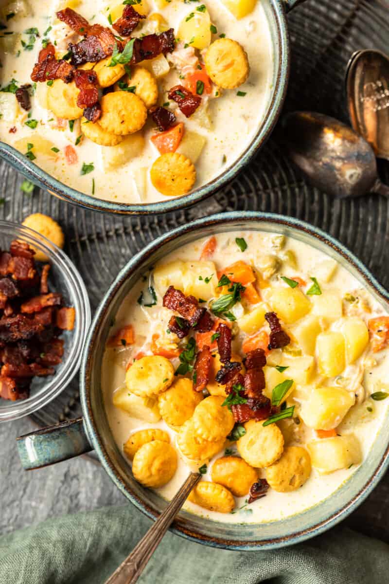 new england clam chowder in gray bowls with oyster crackers and spoons.