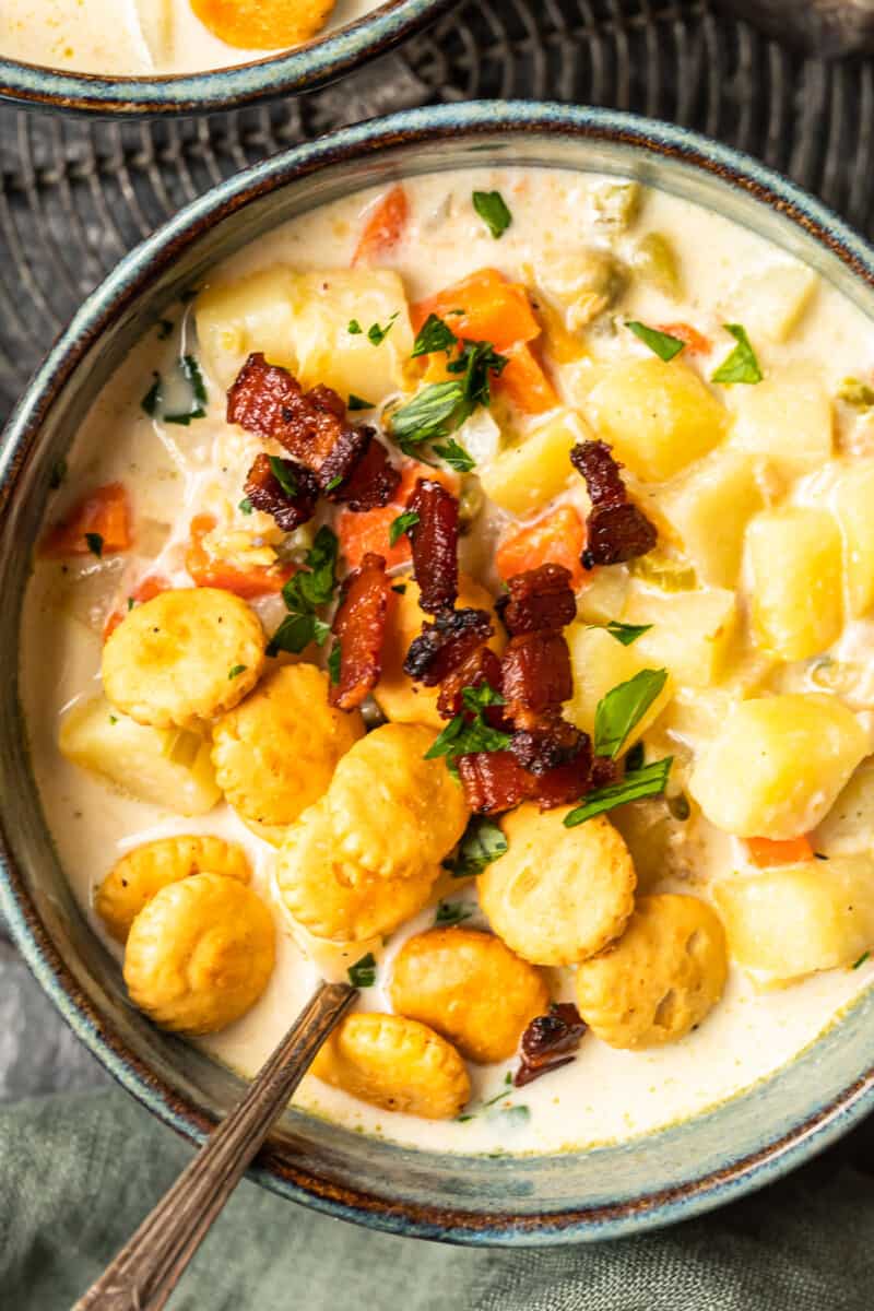 close up on a bowl of thick and cream clam chowder topped with oyster crackers and bacon