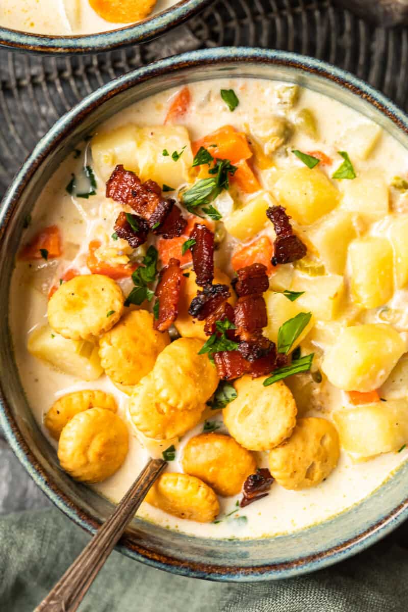 new england clam chowder in a gray bowl with oyster crackers and a spoon.