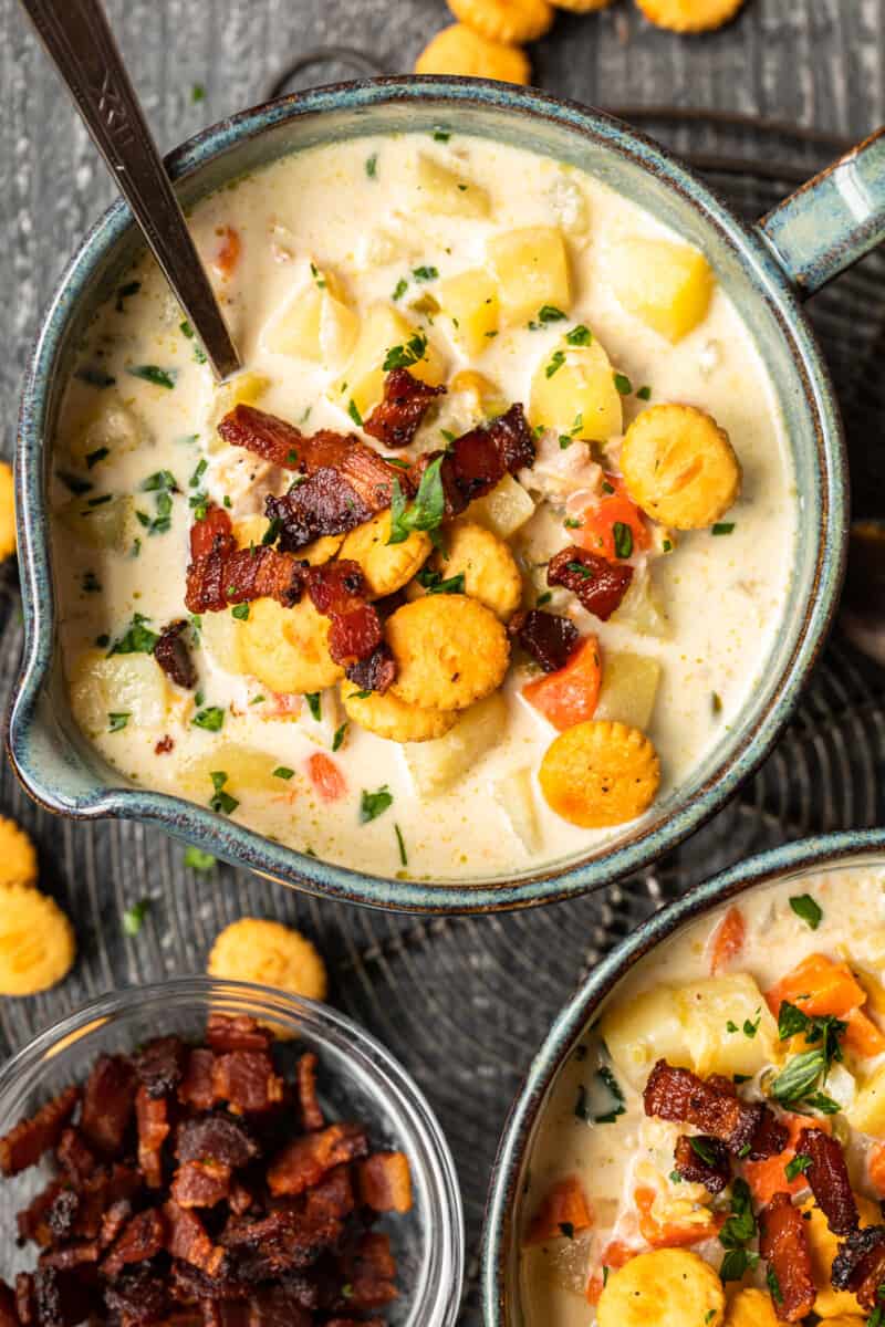 An overhead image of clam chowder bowls on a table with extra cup of crispy bacon.