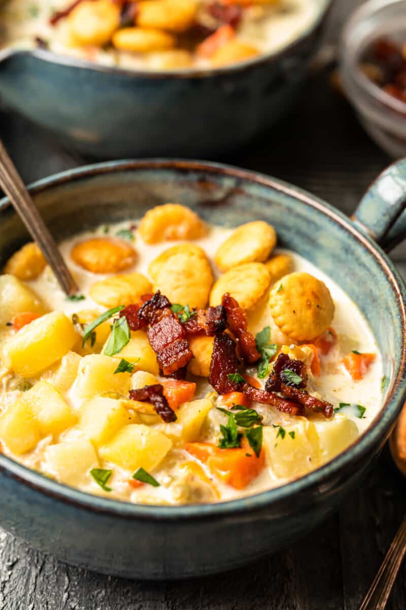 new england clam chowder in a gray bowl with oyster crackers and a spoon.