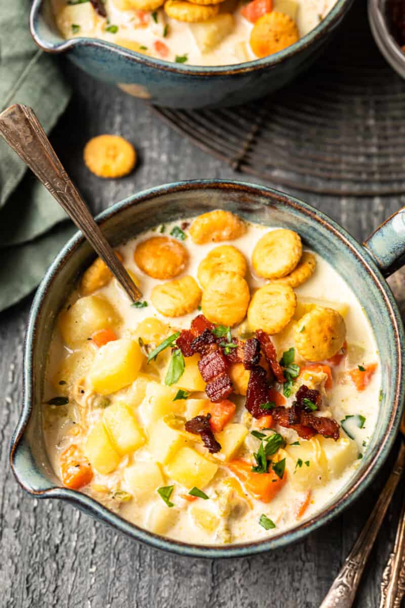 new england clam chowder in a gray bowl with oyster crackers and a spoon.