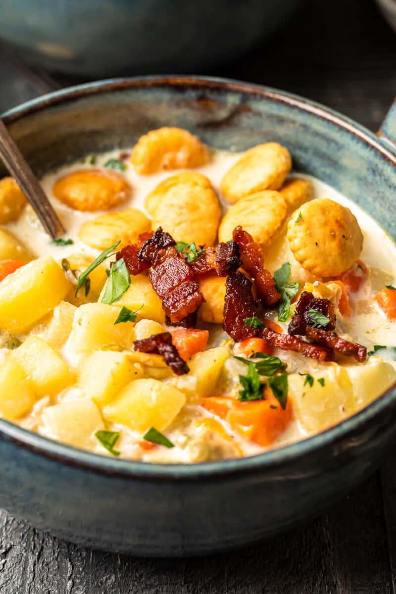 new england clam chowder in a gray bowl with oyster crackers and a spoon.