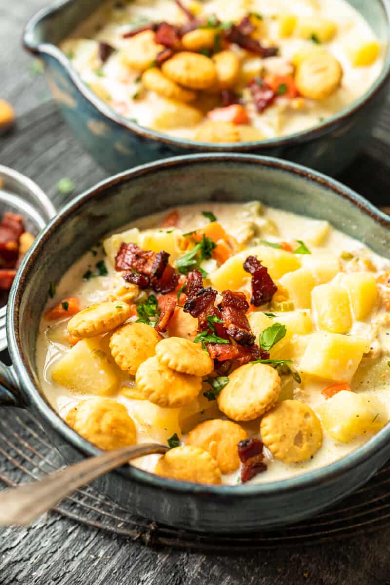 new england clam chowder in gray bowls with oyster crackers and spoons.