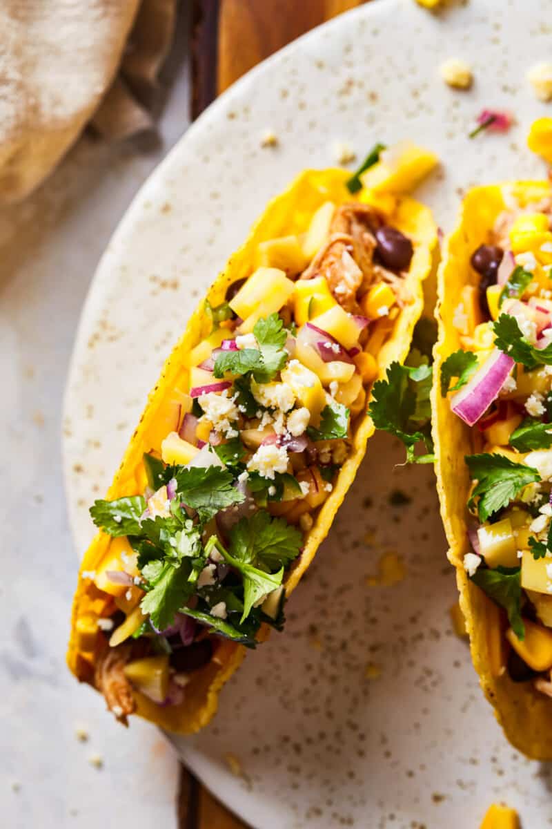 Slow Cooker Chicken Tacos are our favorite easy family dinner recipe! Made with shredded honey BBQ chicken, mango salsa, cilantro, black beans, and cheese for the perfect BBQ Chicken Tacos. slow cooker BBQ chicken tacos