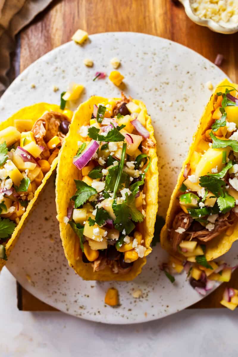 Slow Cooker Honey BBQ Chicken Tacos are our favorite easy family dinner! Top with mango, cilantro, black beans, and cheese for the perfect BBQ Chicken Tacos! SO DELICIOUS! crockpot chicken tacos with mango salsa